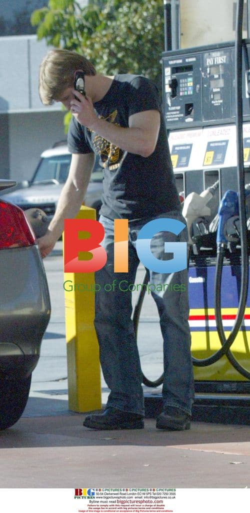 Benjamin Mackenzie pumping gas, using phone